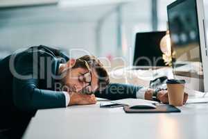 The busy day has knocked him out. a tired young businessman sleeping on his desk inside of the office during the day.