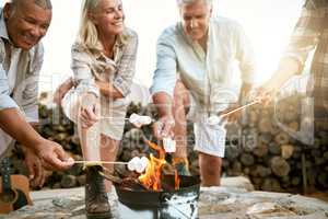 Camping, hiking and adventure senior people melting marshmallows in a camp fire during a nature retreat or getaway outdoors. Happy retired or senior group of friends enjoying fun recreation activity