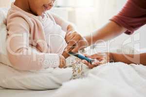 Testing glucose, blood pressure and diabetes of little girl with insulin treatment in bed at home. Mother checking health, wellness and blood sugar medical measurement of her daughter in a bedroom