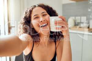 Happy, morning coffee and selfie while smiling and holding cup against her face for warmth while sitting at home. Portrait of a cheerful young woman enjoying her free time and a hot beverage