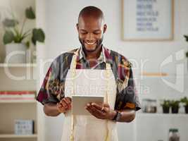 . Fashion designer, tailor and textile workshop employee browsing and looking at a design on a tablet in a trendy and stylish small business. Checking an online clothing order on his company website.