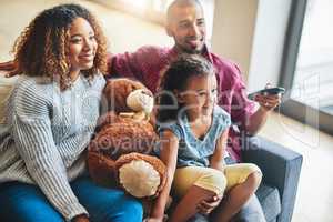 Parenthood is choosing family friendly films for a Sunday afternoon. a happy young family of three watching tv from the sofa at home.