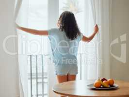 Awake, waking up and fresh new day or morning for a young woman opening the curtains. Back view of a carefree female with hope thinking while looking out the window in her house or at home