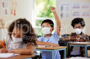 School student raising hand to volunteer, participate and answer question at class lesson in covid pandemic. Curious, smart and clever young boy wearing a mask for education and learning