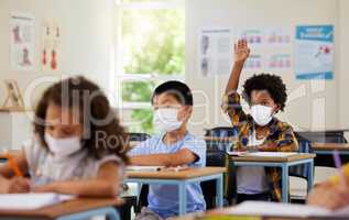 Covid, students and education children in school classroom raising hand to answer, ask or question lesson with classmates. Diverse group of kids, boys or girls with face masks learning in study class
