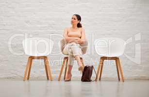 Employment, hiring and recruitment with a young business woman sitting on a chair waiting for her interview with human resources. Female shortlist candidate looking impatient or nervous for a meeting