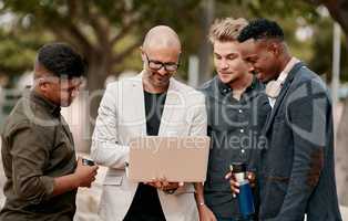 A team leader coaching his staff outdoors, standing and using a laptop. A group of male designers working on a start up project, looking at content on a computer outside, teamwork in the open air.