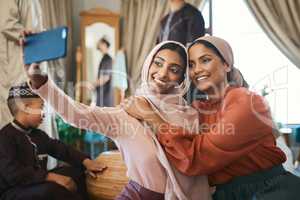 Muslim sisters taking selfies in traditional Islamic head scarf inside a happy family home together. Beautiful young women who are proud of their religion post photos of Eid Ramadan on social media