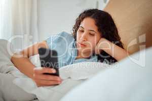 Young woman checking phone and social media in bed, browsing internet after waking up to text message at home. Female relaxing, chatting online and streaming. Lady feeling lazy on the weekend
