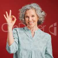 Good, perfect and okay with a senior woman hand gesture or sign in support or positive backing in studio against a red background. Portrait of a mature female looking motivated, happy and smiling