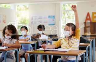 Wearing face mask to protect from covid while learning in class, answering education question and studying with students in a classroom. Girl sitting at a desk and raising hand during a pandemic