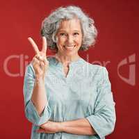 .. Senior woman express peace sign, v gesture and emoji with fingers on red studio background. Portrait of carefree, cool and smiling lady in positive, playful and fun mood showing victory with hand.