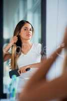 Combing her hair for a soft and sleek style. an attractive young woman brushing her hair in the bathroom.