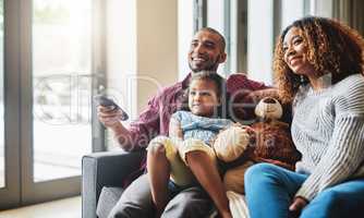 Looks like your favourite show is on sweetie. a happy young family of three watching tv together in their living room at home.