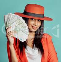 Rich, successful and wealthy young woman holding cash money after winning competition, lottery or casino prize. Smiling, elegant and trendy female with pay reward against a blue studio background