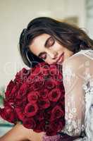 What a comfortable way to spend the day. a beautiful young woman holding and resting with her face on a bouquet of roses that she bought.