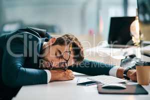 He is one hard working guy. a tired young businessman sleeping on his desk inside of the office during the day.