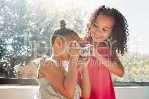 Cute sisters bonding, taking photos on camera at home, smiling while being playful and curious. Little girls playing, having fun together, enjoying their bond and sharing precious childhood moments