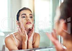 Keeping her skin in fabulous condition. an attractive young woman inspecting her skin in the mirror.