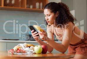 Woman reading phone, researching a diet with fresh fruit while relaxing in a kitchen at home. Young female searching for a recipe, cleanse or detox online. Lady checking nutritional value of a banana