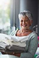 Anybody call for freshly washed towels. Portrait of a mature woman holding freshly folded towels while doing laundry at home.