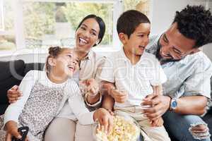 Family watching tv or a movie, having fun and eating popcorn together at home. Love and laughter with affectionate parents and happy children smiling, enjoying the weekend and feeling carefree