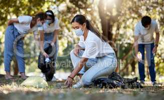 Group of volunteers picking up, cleaning and reducing pollution in a public nature park together. Diverse community wearing face masks to protect from disease, collecting dirt and doing cleanup