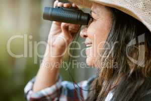 . Nature, animal and bird watching of a smiling older woman looking and holding binoculars outside. Closeup of a mature female enjoying retirement relaxing on a day outdoors break feeling carefree.