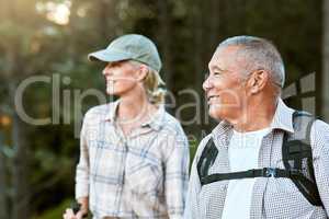 Mature man and woman hiking, smiling and looking at the view in nature. Fit local travel guide showing an active female tourist the natural landscapes while walking a trail outdoors in the wilderness