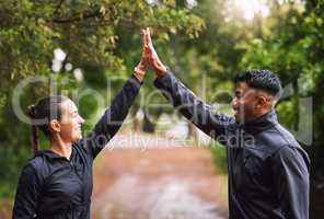 Athletic couple high five while exercising in a park or forest, celebrating and winning before a run. Fit boyfriend and girlfriend bonding while keeping fit and healthy. Fun lovers being active
