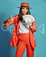 Rich woman showing off wealth, going on shopping spree and winning the lottery standing against blue studio background. Portrait of a stylish, trendy and happy female millionaire holding a cash prize