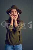 Shout your heart out. Studio shot of a carefree young woman posing with a hat while standing against a dark background.