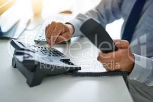 Hes ready to assist. an unrecognizable businessman dialing a number on a telephone at work.