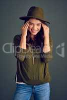 Even hats look good on her. Studio shot of a cheerful young woman posing with a hat while standing against a dark background.