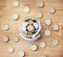 . Savings, investment and a jar full of coins on a wooden table for future financial growth or insurance. Overhead view of an overflowing container with money for a donation or retirement fund.