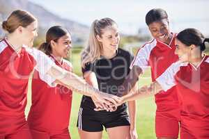 Female only soccer team joining hands in a huddle in unity, support and trust before a match or competition. Happy group or squad of womens football players on a field standing in a circle