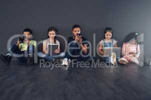 Learning to be technology literate. Studio shot of kids sitting on the floor and using wireless technology against a gray background.