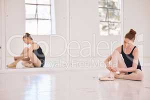 Female ballet dancer preparing pointe shoes in a ballet hub, studio or class with mirror reflection of her sitting on the floor. Young, single ballerina performer getting ready for practice rehearsal