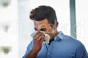 He needs an immune booster for his defense against flu. a young businessman blowing his nose at work.