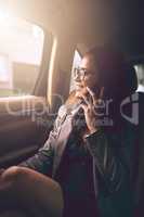 Keeping success in motion. a young businesswoman talking on a cellphone in the backseat of a car.