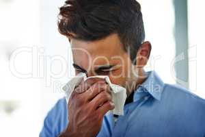 Flu season is on its way. a young businessman blowing his nose at work.