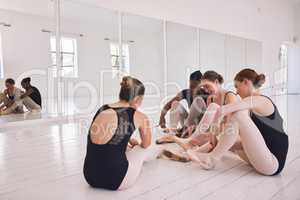 Group of female ballet dancers getting ready or dressing in a ballet hub, studio or class. Young, cheerful ballerina performer girls putting on pointe shoes and body suit inside a modern dance center