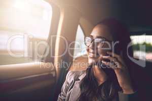 Ill be in the office shortly. a young businesswoman talking on a cellphone in the backseat of a car.