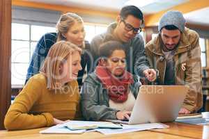 Everyone trying to solve a problem together. a cheerful young group of students working together using a laptop to study for exams inside of a library.