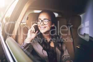 Im heading to the office right now. a young businesswoman talking on a cellphone in the backseat of a car.