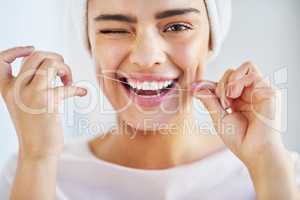 Go the extra mile for your smile. Portrait of a beautiful young woman flossing her teeth in the bathroom at home.