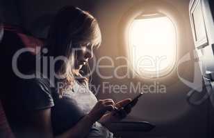 Connected, even in the air. an attractive young woman texting while sitting in an airplane.