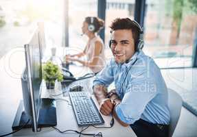 Let us assist you. High angle portrait of a handsome young man working in a call center with a female colleague in the background.