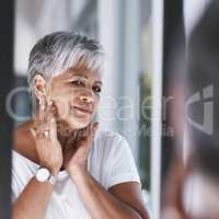 No spots no imperfections. a cheerful mature woman touching her face with her hands while looking at her reflection in a mirror.