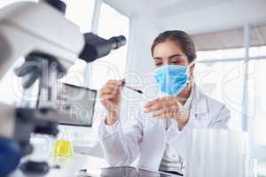 Just one tiny little drop. a focused young female scientist wearing a surgical mask and doing an experiment while being seated inside a laboratory.